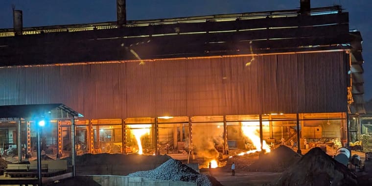 Molten alloy tapped from the furnaces at dusk, seen through the open side of the furnace building