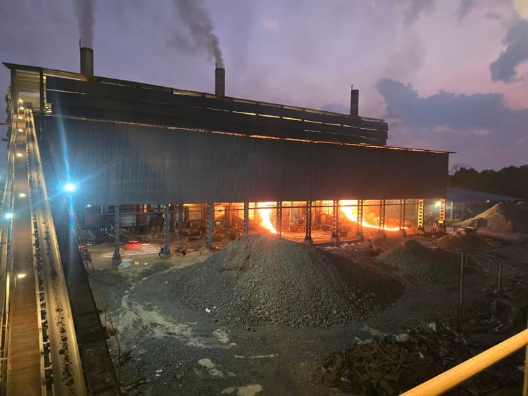 The works at dusk: the charging conveyor climbing to the furnace building, stacks smoking, the tap glow running the length of the bays