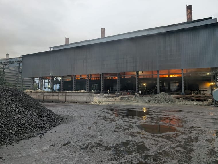 Manganese ore stockpiled in the yard in front of the furnace shed, with the tap glow showing between the columns