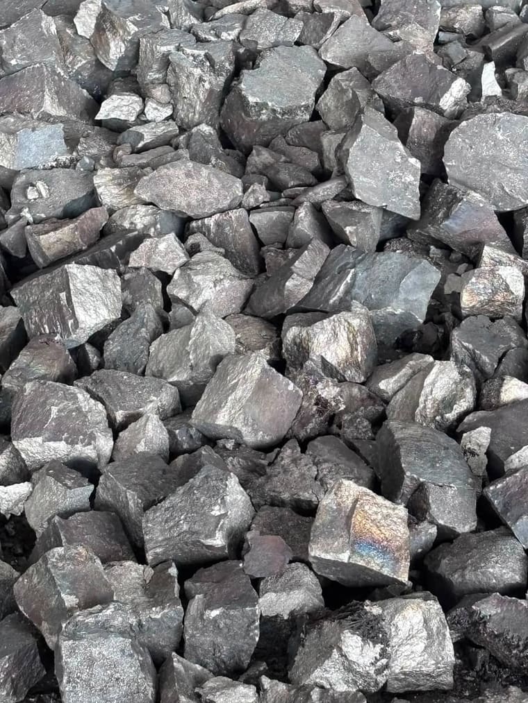 Crushed and sized ferro alloy in a stockpile, bright fracture faces catching the light